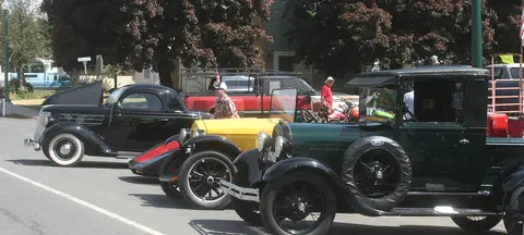 Classic cars parked along a street with people standing nearby.