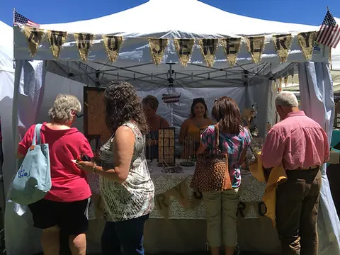People browse a jewelry vendor tent at an outdoor market.