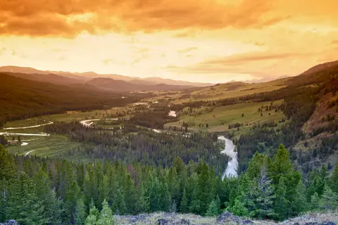 A scenic view of a valley with a winding river and mountains under a warm sunset sky.