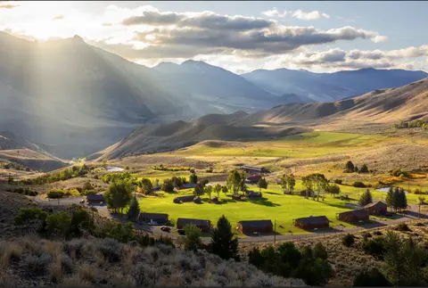 A scenic view of a valley with cabins and mountains in the background under a cloudy sky.