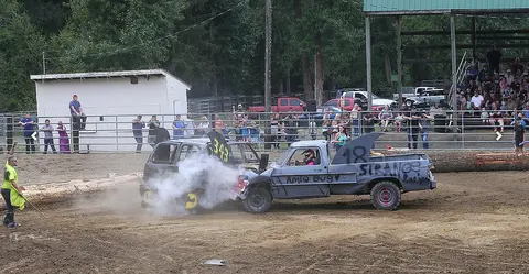 Two cars crash into each other during a demolition derby in an outdoor arena.
