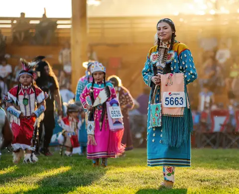 A woman in traditional attire stands outdoors with other people during an event.