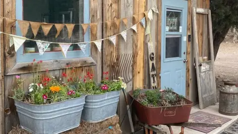 The exterior of a rustic wooden building decorated with flower planters and bunting flags.