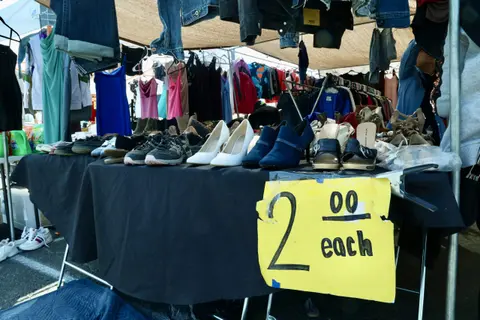 A market stall displays clothing and shoes with a yellow price sign.