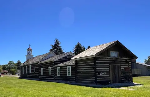 An exterior view of a historic log church under a clear blue sky.