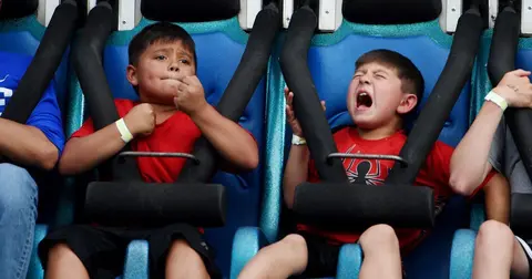 Two boys ride an amusement park ride with intense expressions.