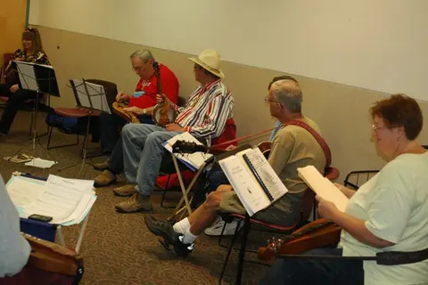 A group of people sitting in a room playing stringed instruments and reading music.