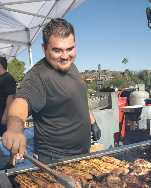 A man grilling food outdoors under a tent.