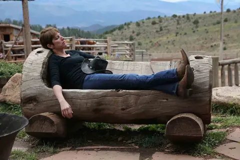 A woman resting on a carved log bench outdoors.