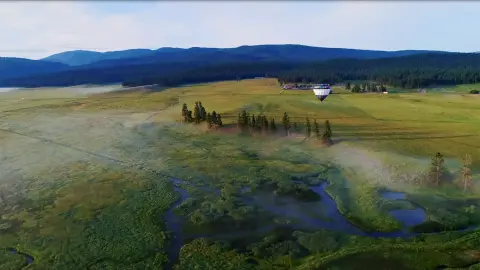An aerial view of a landscape with a hot air balloon flying over green fields and a winding river.