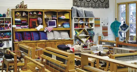 The interior of a weaving and yarn shop with looms and shelves full of textiles.
