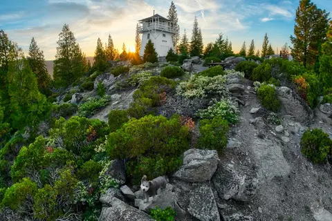 A white lookout tower stands on a rocky hilltop at sunset.