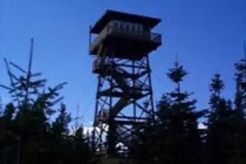 A tall wooden fire lookout tower stands among trees against a blue sky.