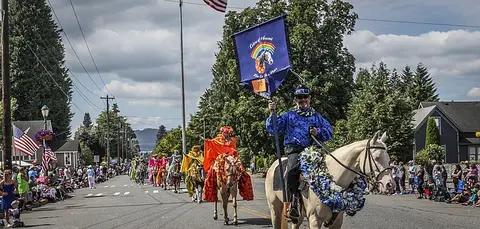 People ride horses adorned with leis in a street parade.