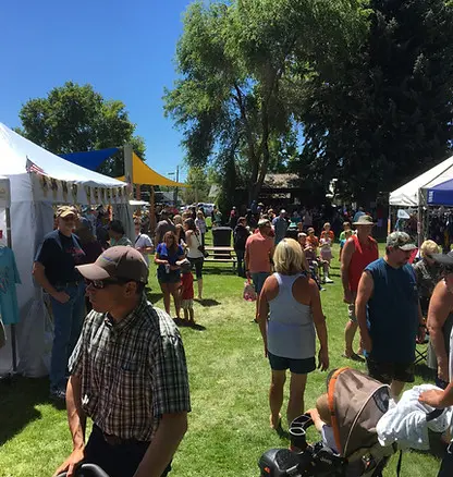 A crowd of people at an outdoor festival with tents and trees.