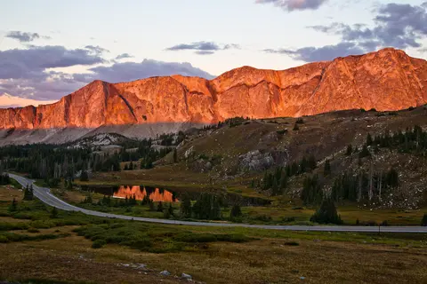 A scenic landscape showing a mountain range illuminated by sunset light with a winding road below.