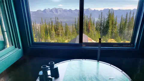 A view of mountains and pine trees through the window of a lookout tower.