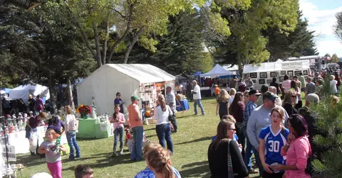An outdoor market or fair with tents and many people browsing booths under trees.