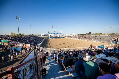 A wide outdoor rodeo arena filled with spectators during an event.