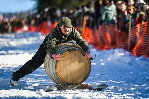 A man rides a barrel attached to skis down a snowy slope in front of a crowd.
