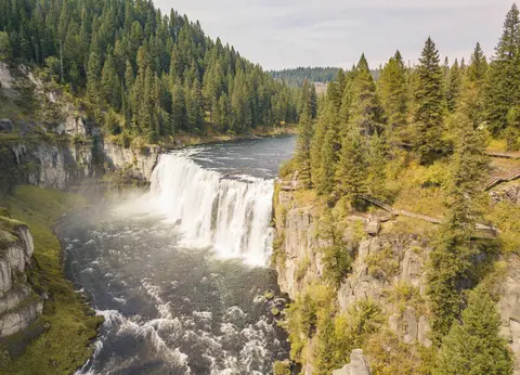 An aerial view of a wide waterfall flowing between rocky, forested banks.