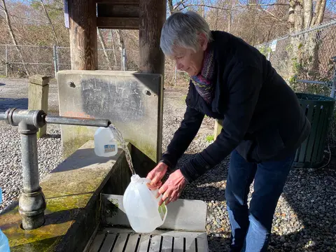 A woman fills plastic jugs with water from an outdoor dispenser.