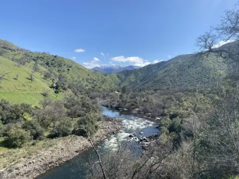 A river flows through a valley surrounded by green hills under a blue sky.