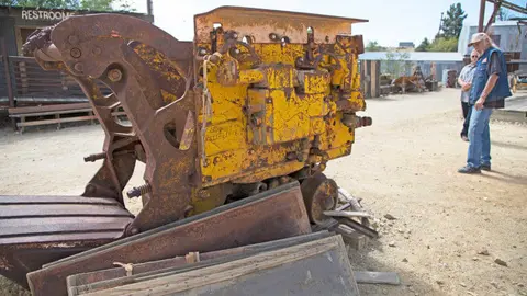 A large rusty piece of mining machinery outdoors with people looking at it.