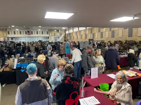 A busy indoor craft fair or flea market with vendors and shoppers.