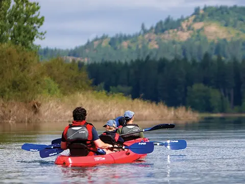 People kayaking on a calm river with hills in the background.