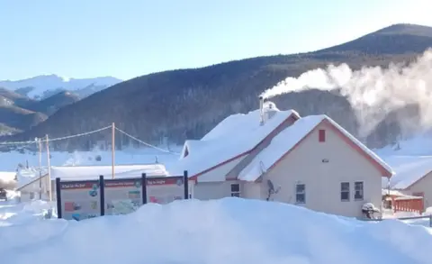 A snowy landscape with a building and mountains in the background.
