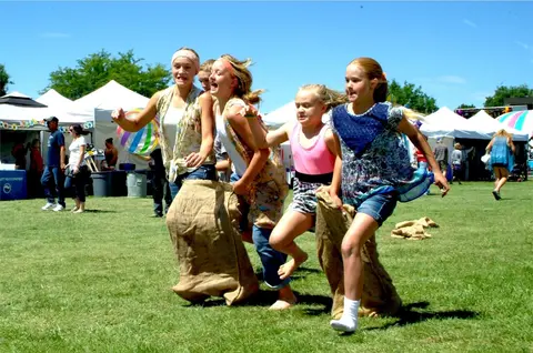 Several children participate in a sack race outdoors on the grass.