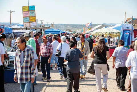 A crowd of people walking through an outdoor market with vendor stalls.