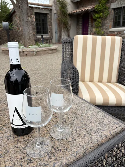 A bottle of wine and two glasses stand on a table outdoors.