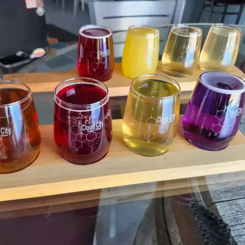 A flight of colorful drinks in branded glasses sits on a wooden paddle.
