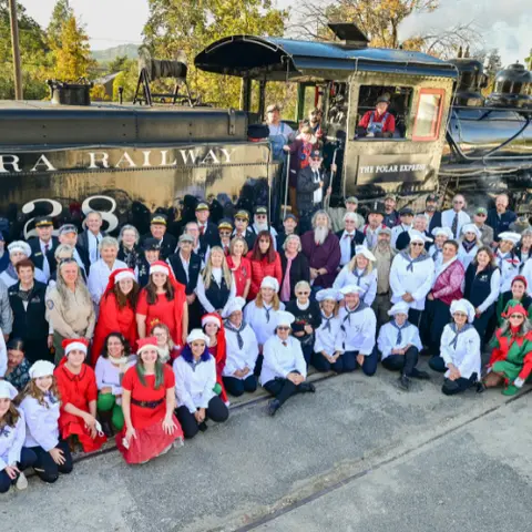 A large group of people pose in front of a steam locomotive.