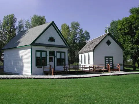 A photo showing two historic wooden white buildings with green trim in a grassy area.