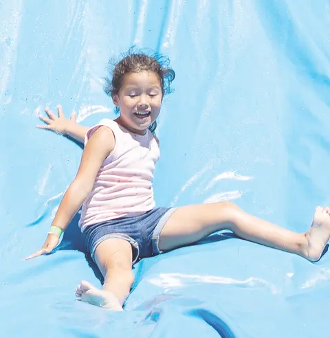 A young girl slides down a blue water slide.