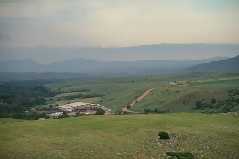 A wide landscape view of green hills and a valley with a building and mountains in the distance.