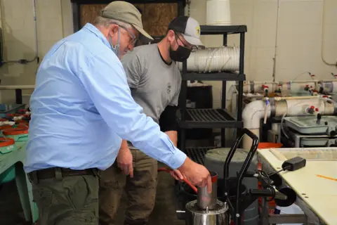 Two men working inside an industrial facility with tanks and pipes.