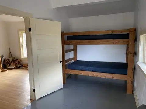 A small room with a wooden bunk bed and an open door leading to another room.