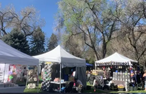 Vendor tents are set up outdoors in a park area with trees.