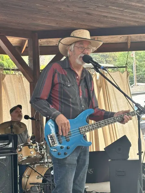 A man playing bass guitar and singing into a microphone on a stage.