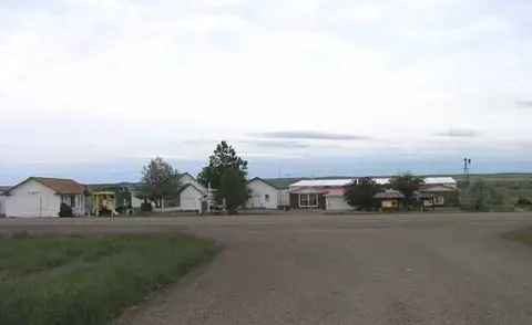 An exterior view of small buildings along a dusty road under an overcast sky.