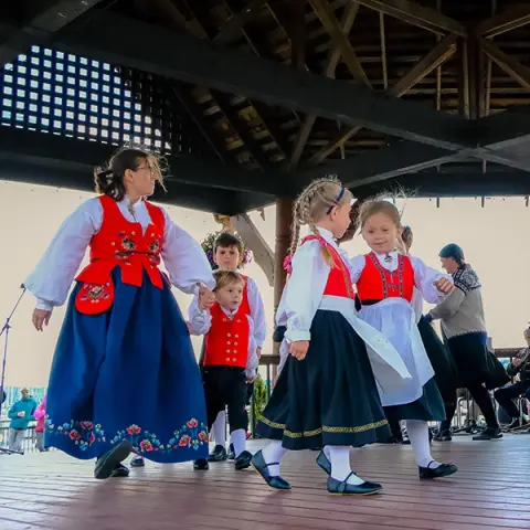 People in traditional costumes dance on a wooden stage.
