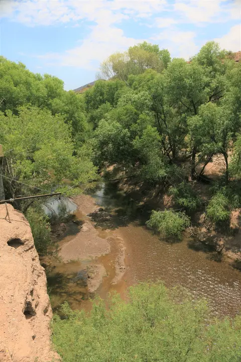 A river flows through a lush, green landscape with rocky banks under a cloudy sky.