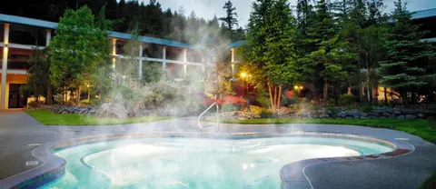 A steaming outdoor pool sits in front of a building surrounded by trees.
