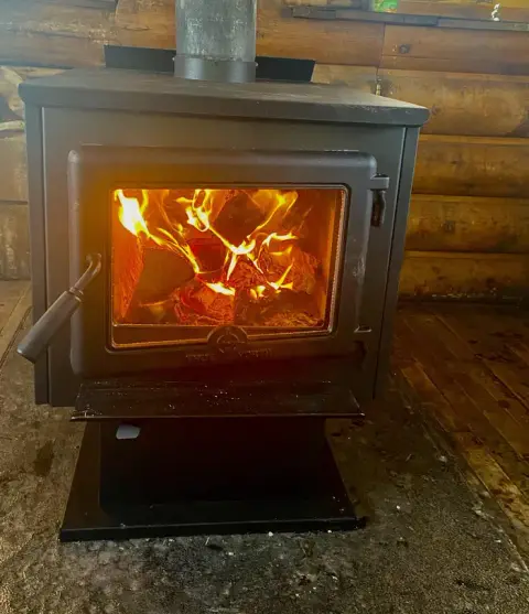 A wood-burning stove is lit inside a rustic cabin.