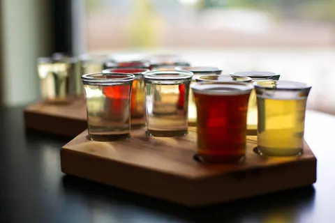 A flight of drinks in small glasses rests on a wooden paddle.