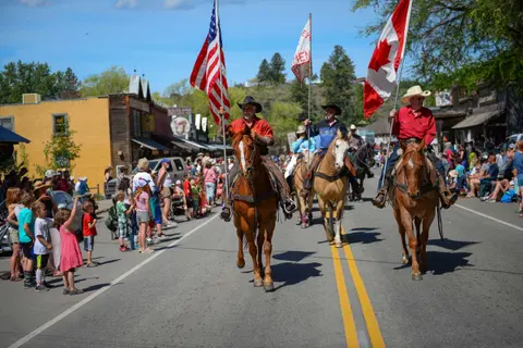 People on horseback carry flags in a parade down a street.